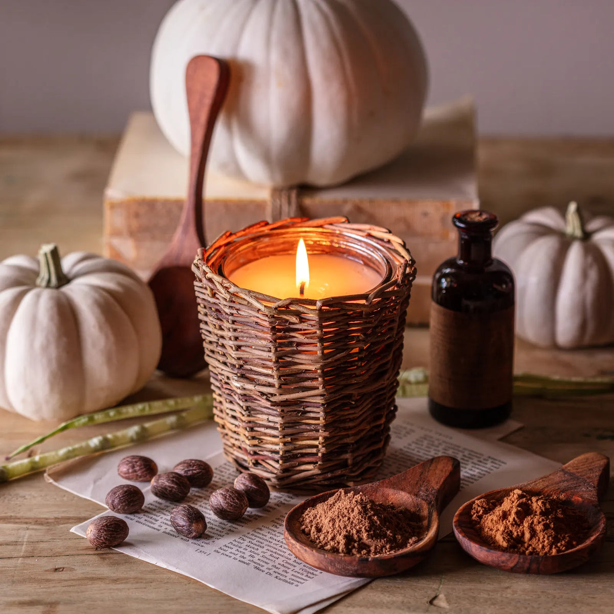Wicker pumpkin candle lit on a wooden table with white pumpkins and spices